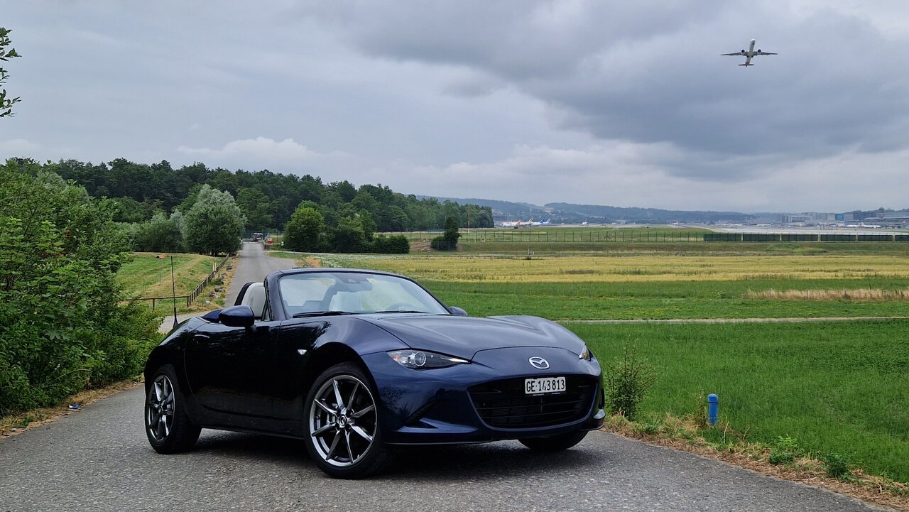 Der Mazda MX-5 von vorne mit einem startenden Flugzeug im Hintergrund