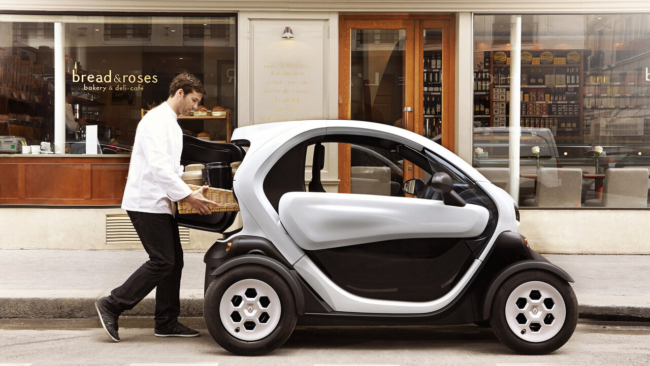 Seitenansicht des Renault Twizy, während ein Mann ein Paket in den Kofferraum lädt.