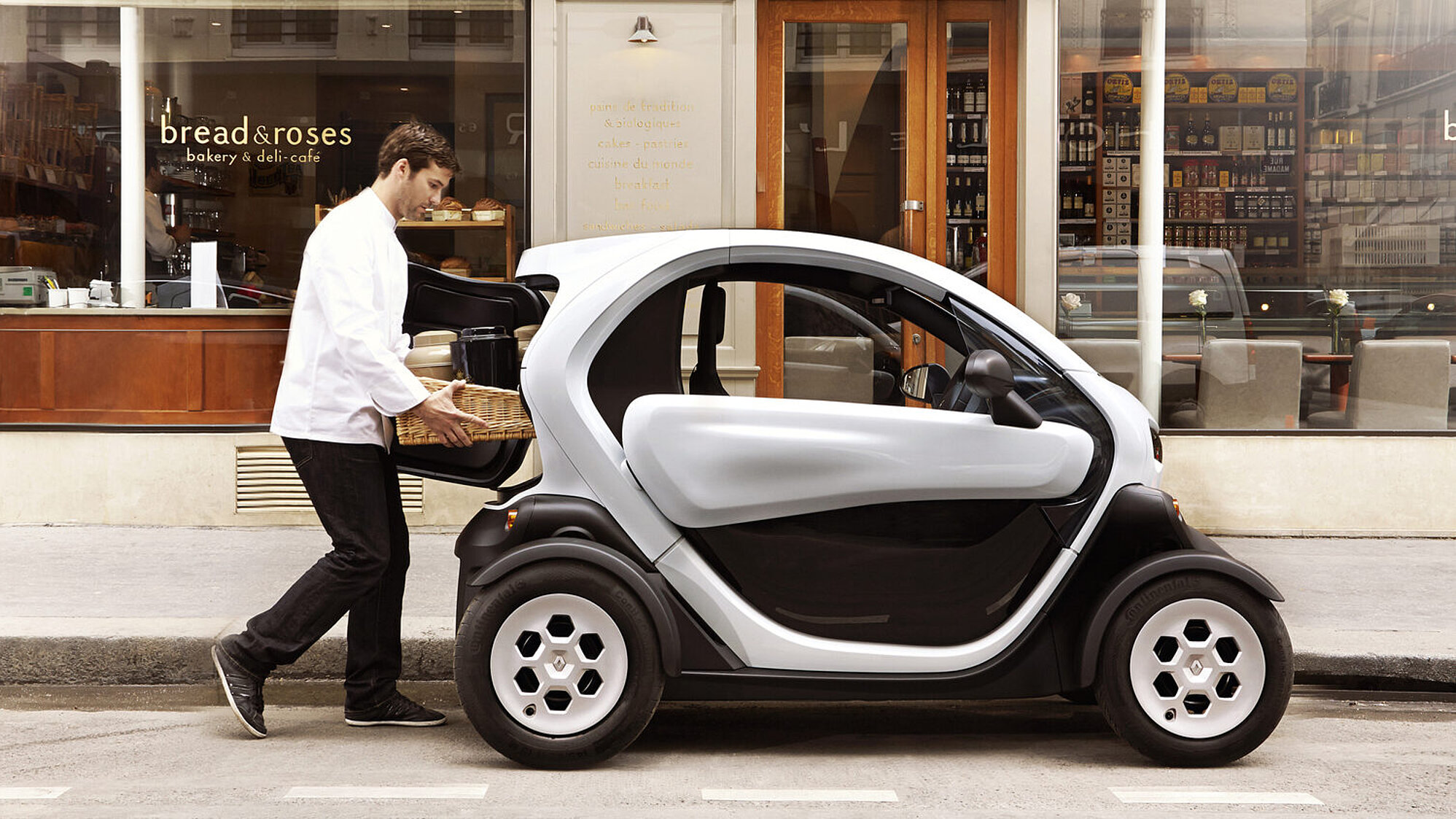 Seitenansicht des Renault Twizy, während ein Mann ein Paket in den Kofferraum lädt.
