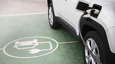 Elektroauto Icon am Boden neben Auto welches eingesteckt ist