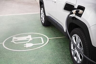 Elektroauto Icon am Boden neben Auto welches eingesteckt ist