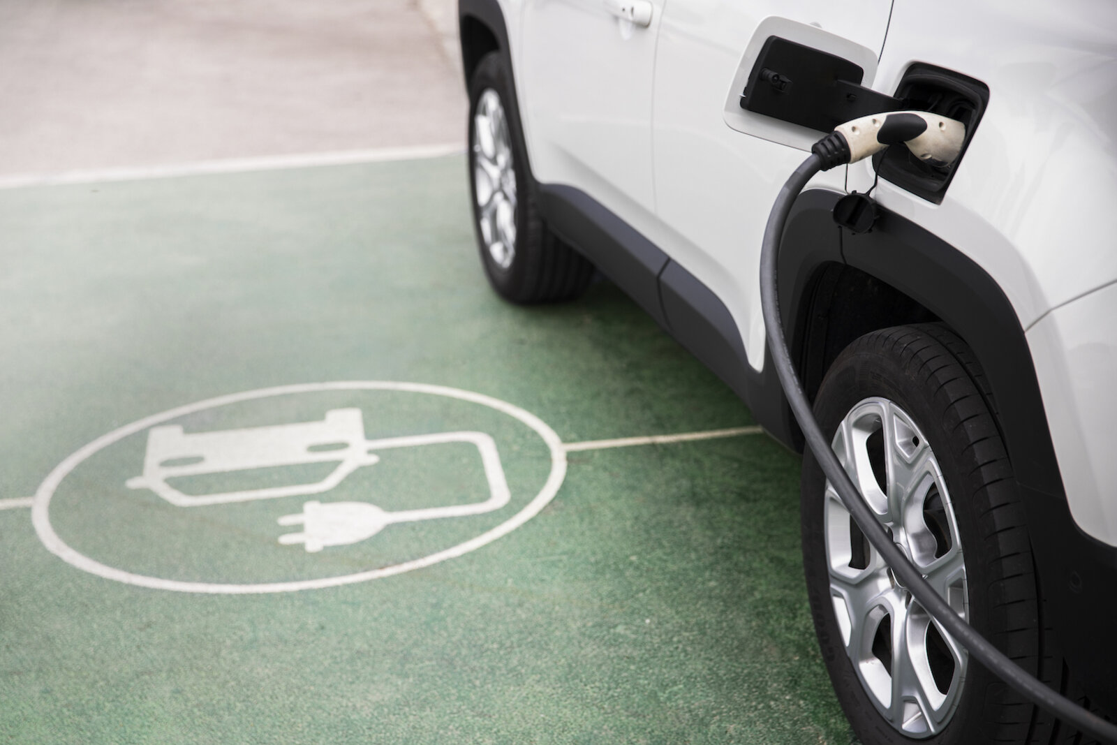 Elektroauto Icon am Boden neben Auto welches eingesteckt ist