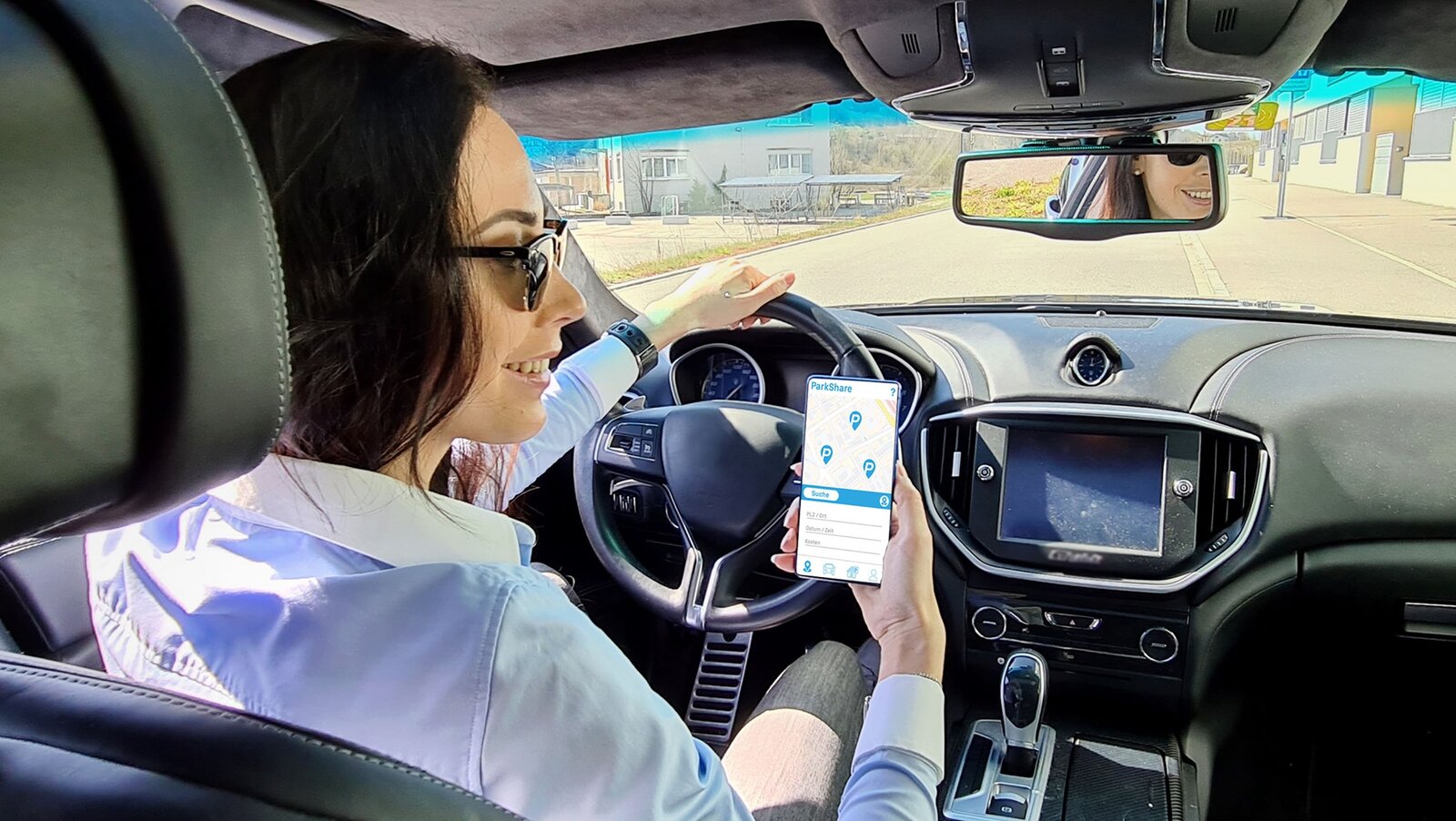 Eine Frau steht am Strassenrand und sucht auf ihrem Smartphone einen Parkplatz.