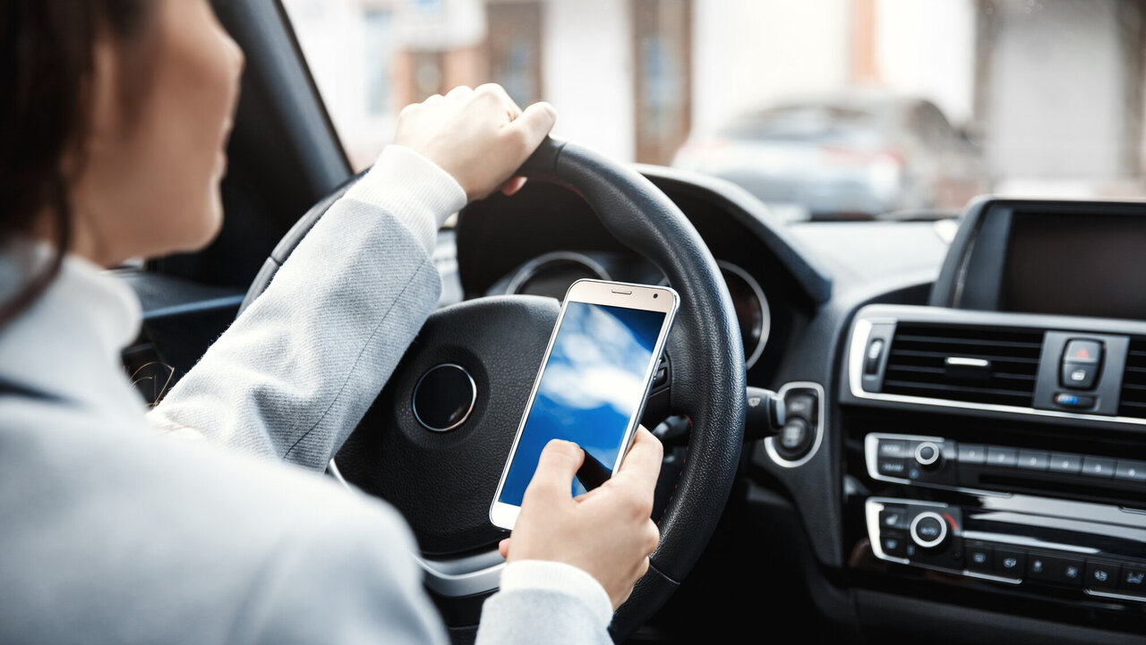 Person nutzt Handy am Steuer ihres Autos