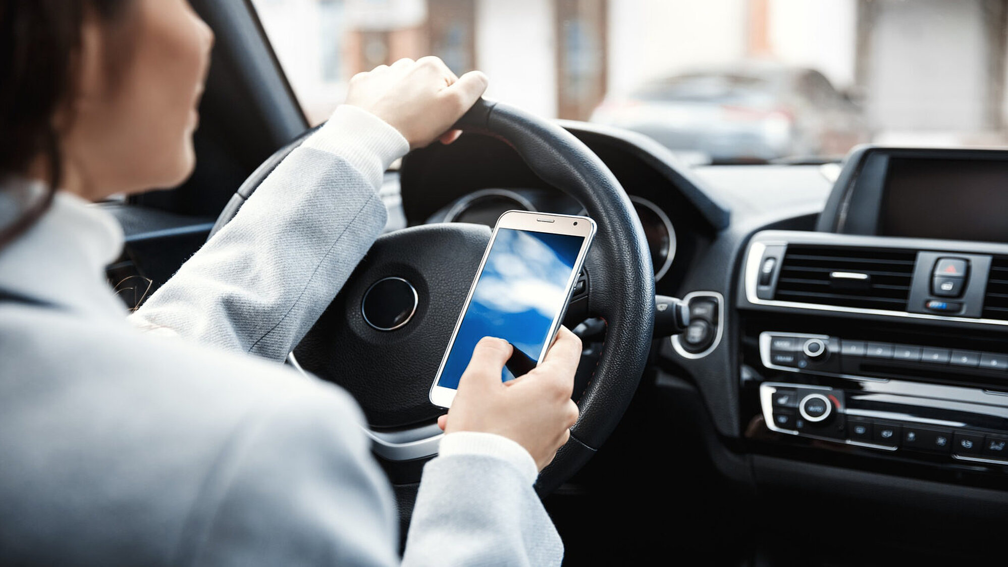 Person nutzt Handy am Steuer ihres Autos