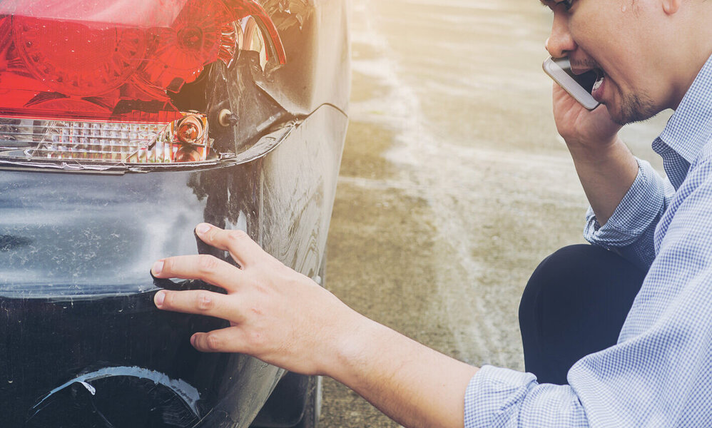 Ein Mann begutachtet einen Unfallschaden