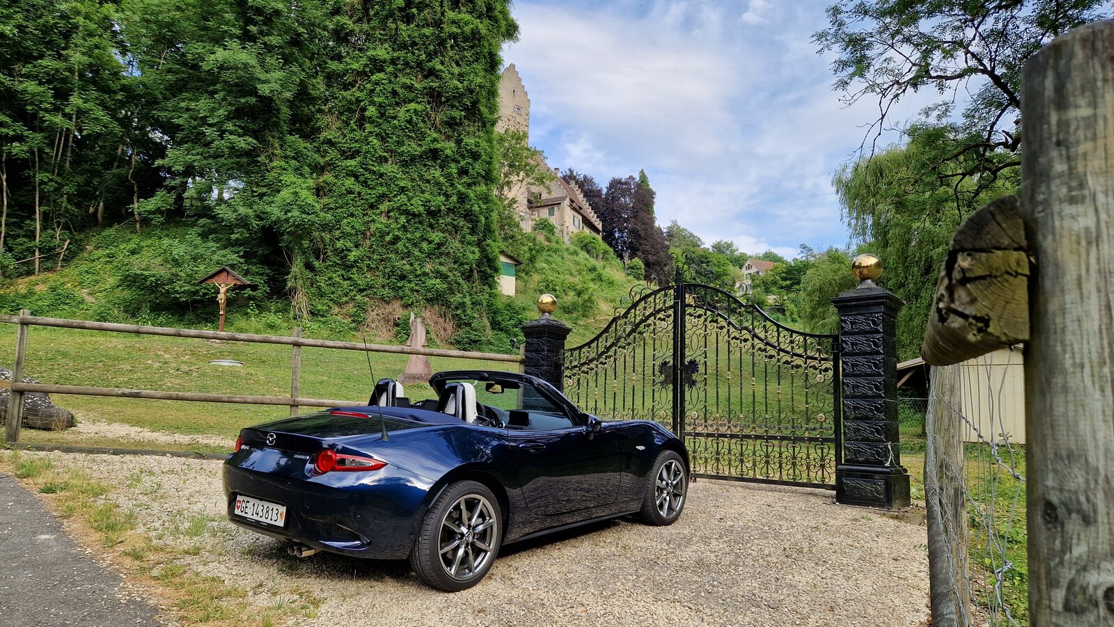 Der offene Mazda MX-5 in der Heckansicht vor dem Tor eines Landgutes.