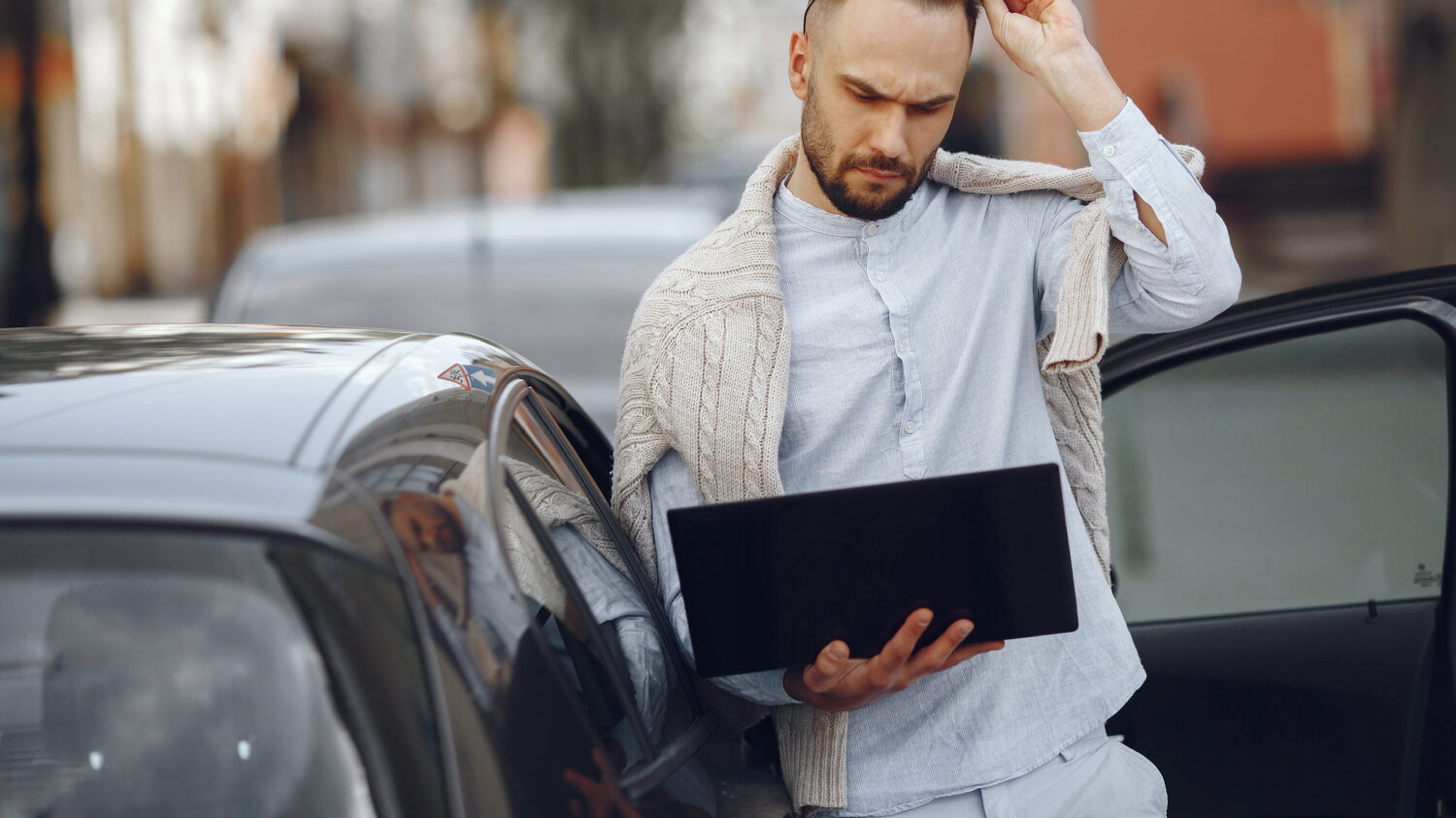 Mann neben Auto mit Laptop.