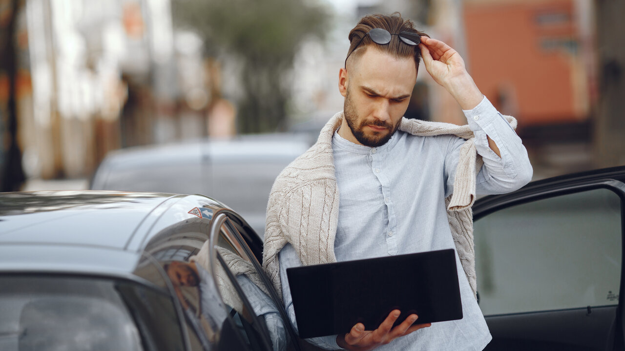 Mann neben Auto mit Laptop.