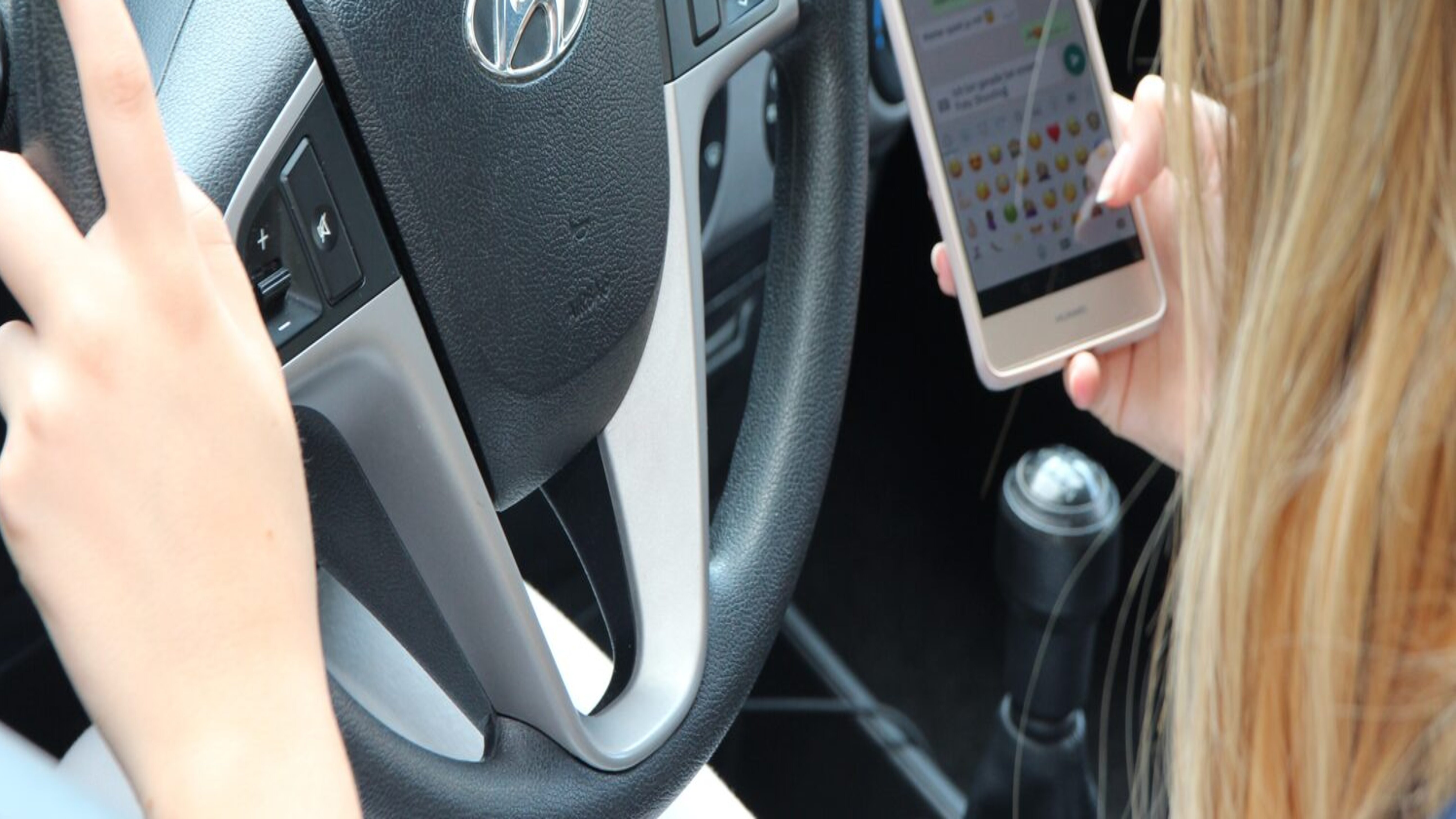Frau am Steuer mit Handy in der Hand
