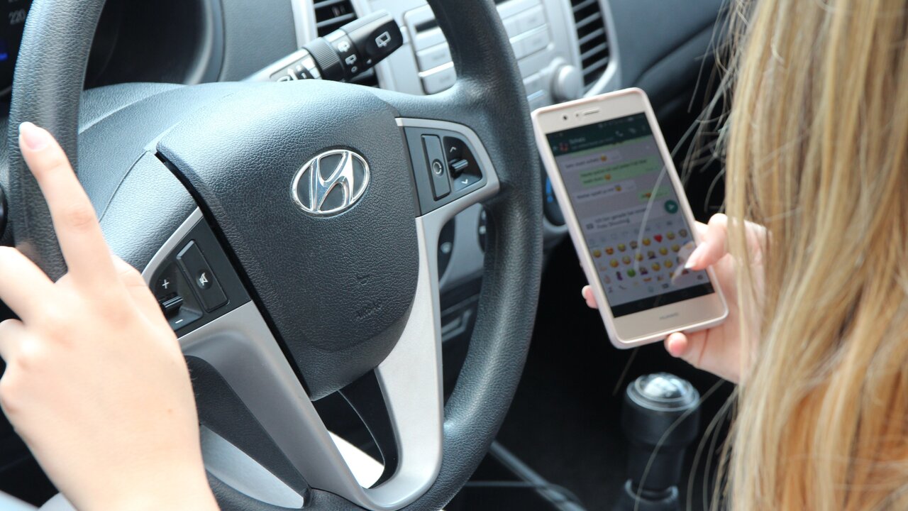Frau am Steuer mit Handy in der Hand