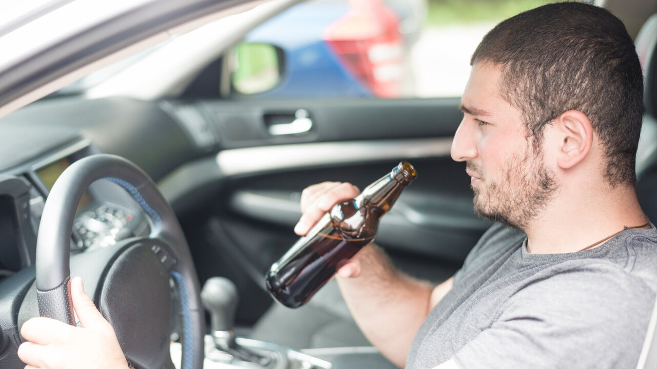 Ein Mann trinkt ein Bier während der Fahrt