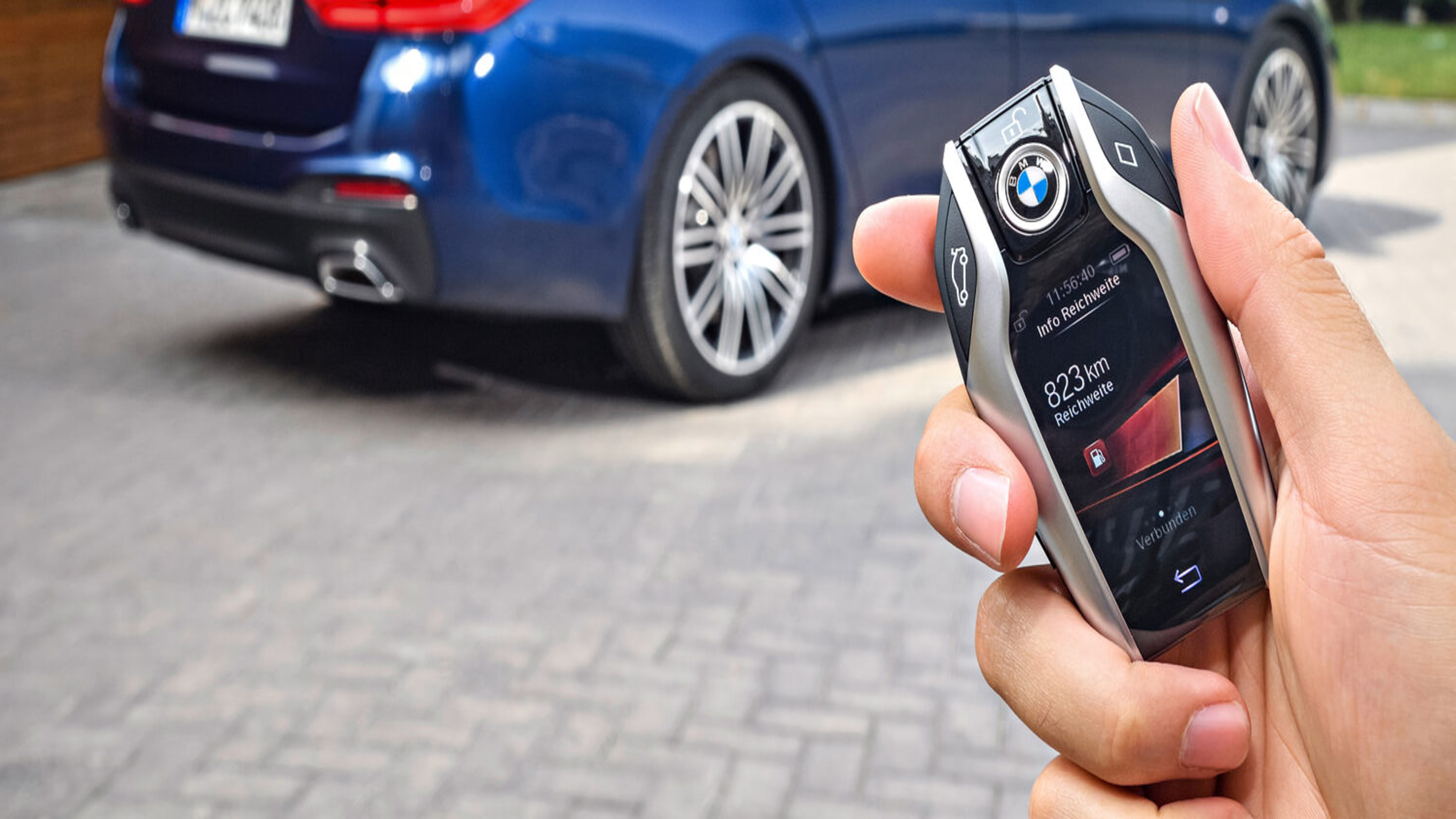 BMW Keylessschlüssel in einer Hand im Hintergrund ein BMW Kombi