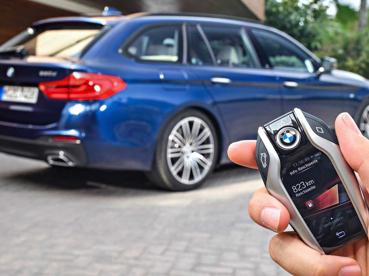 BMW Keylessschlüssel in einer Hand im Hintergrund ein BMW Kombi