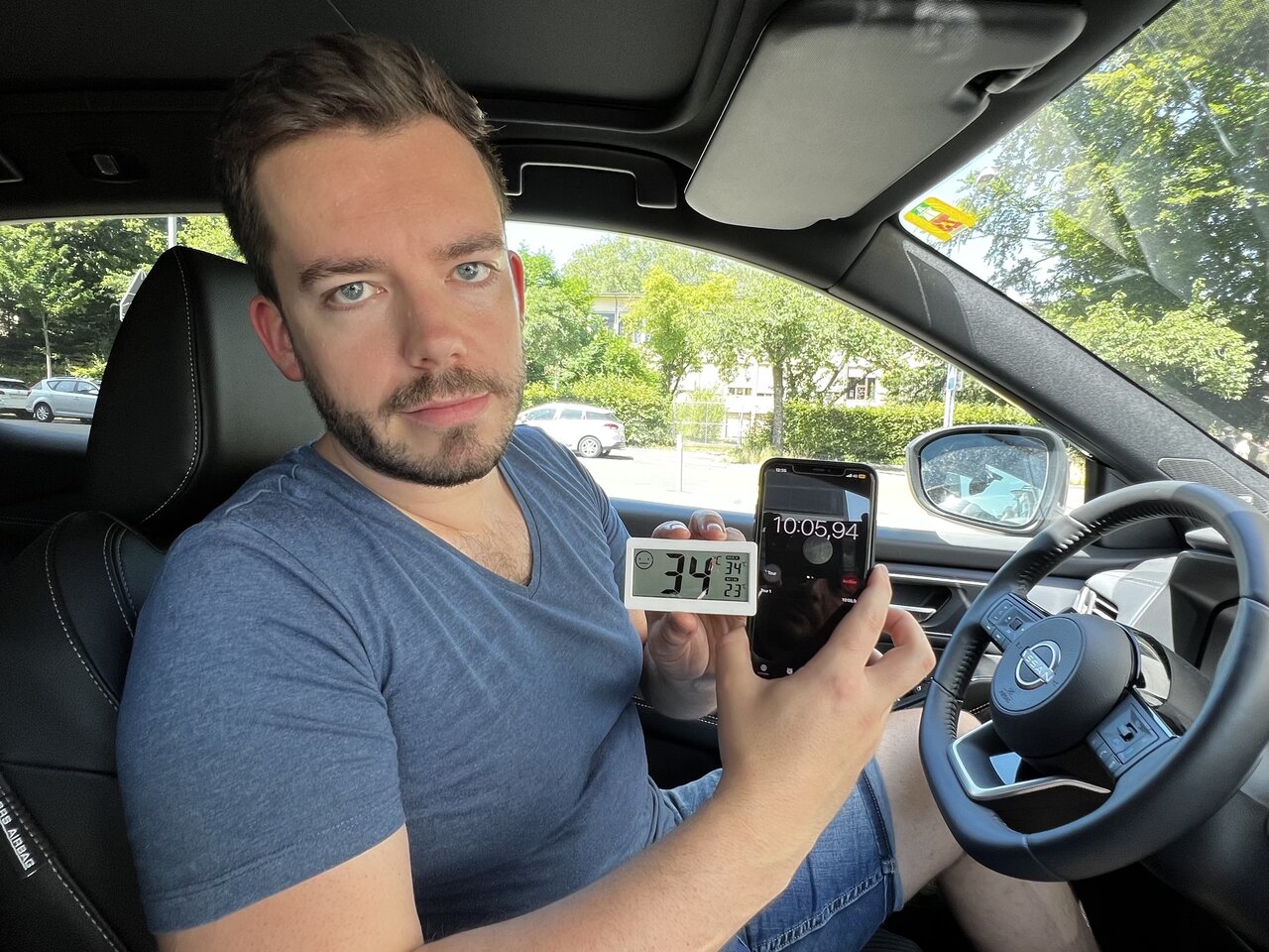 Redaktor Linus Barta mit Thermometer und Telefon in der Hand im Auto