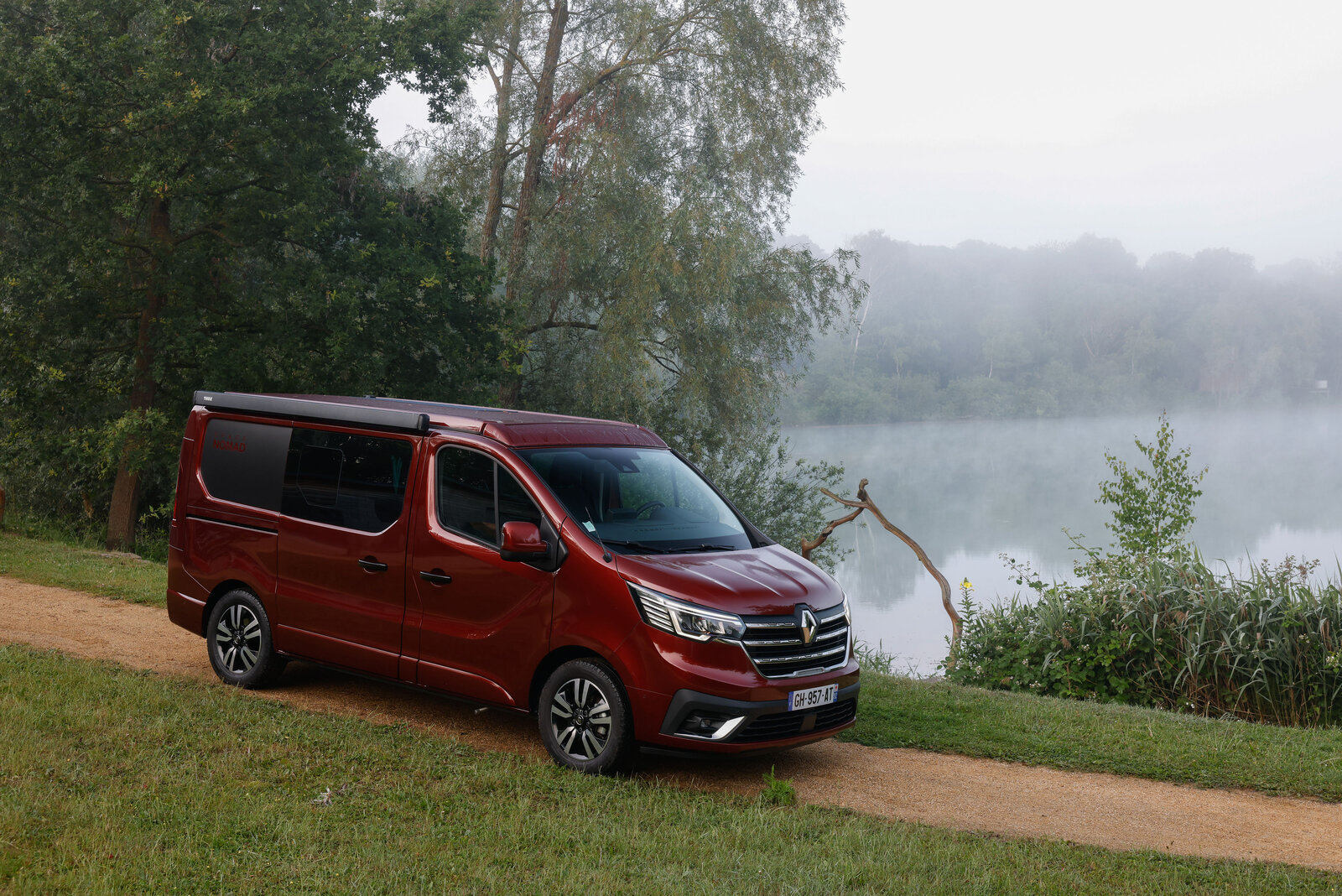 Der Camper Renault Trafic Spacenomad steht abfahrbereit an einem See.
