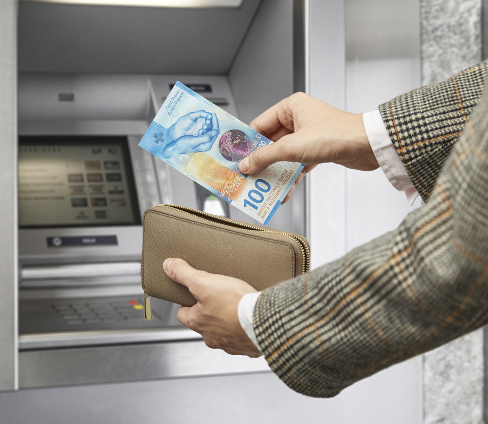 Ein Mann hebt am Bankomat 100 Franken ab