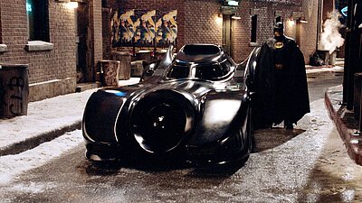 Michael Keaton als Batman neben dem Batmobil aus dem Film von 1989.
