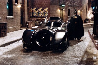 Michael Keaton als Batman neben dem Batmobil aus dem Film von 1989.