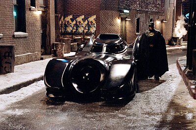 Michael Keaton als Batman neben dem Batmobil aus dem Film von 1989.