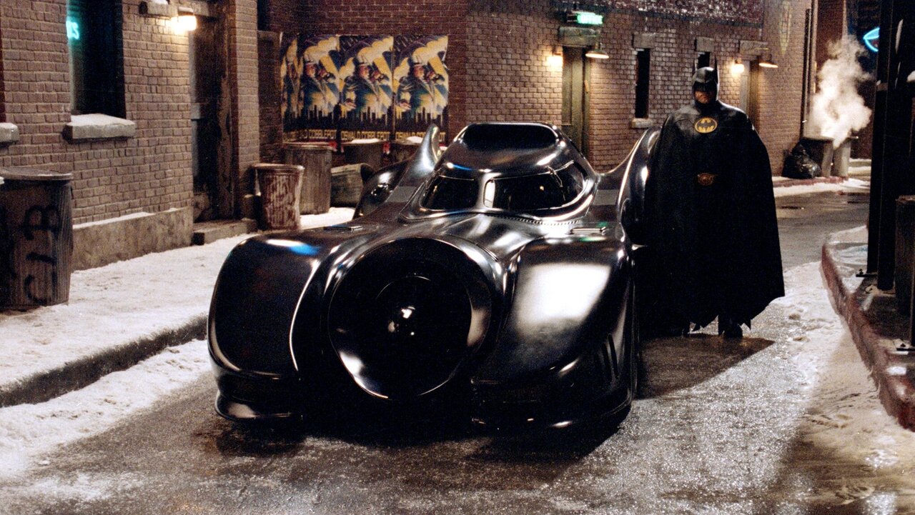 Michael Keaton als Batman neben dem Batmobil aus dem Film von 1989.