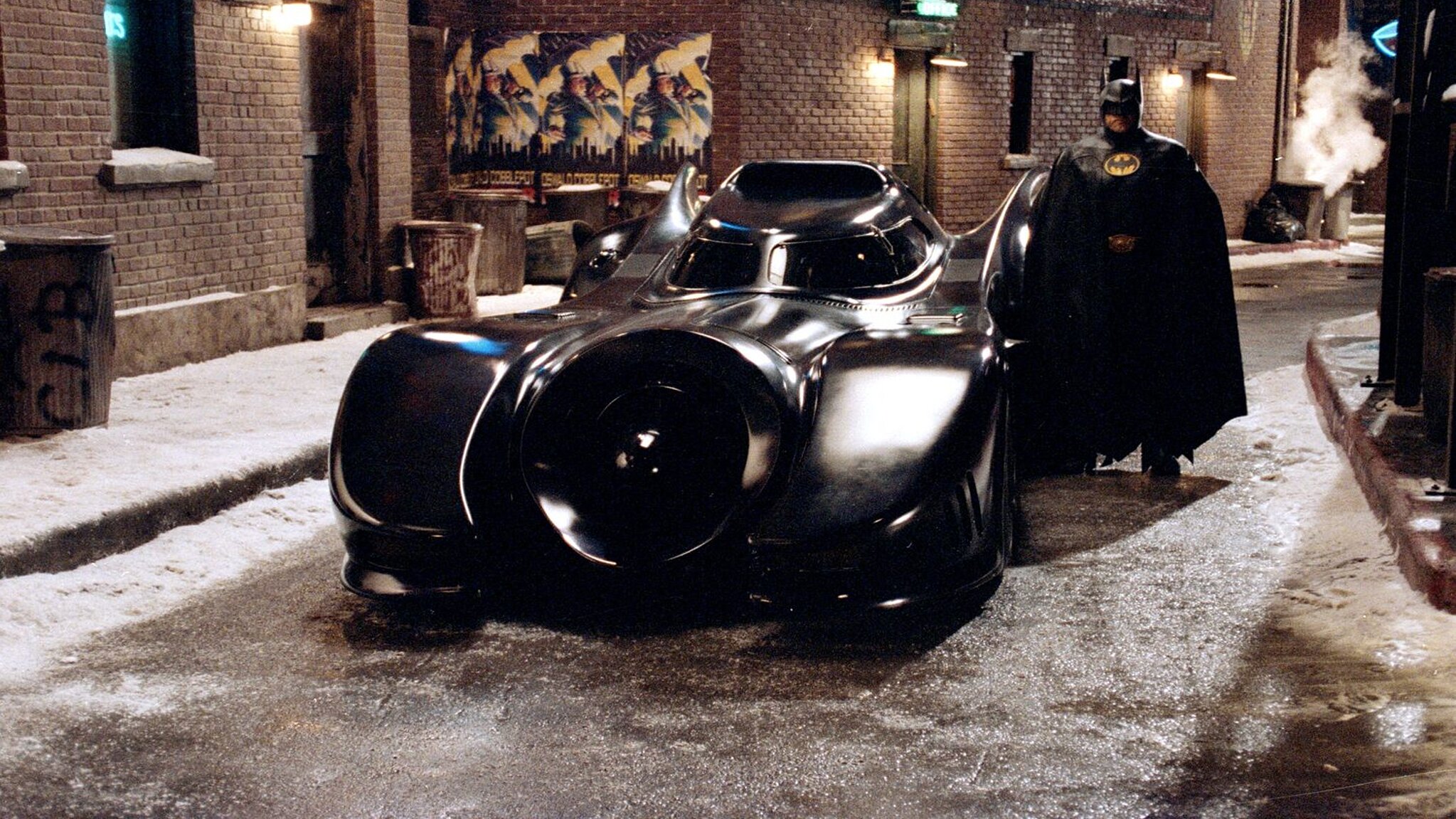 Michael Keaton als Batman neben dem Batmobil aus dem Film von 1989.