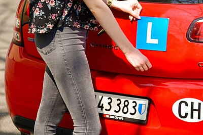 Eine Person bringt das L am Heck eines Autos