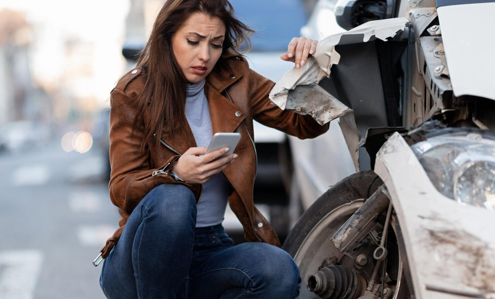 An Frau kniet neben ihrem beschädigten Auto
