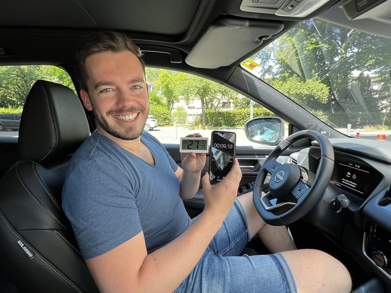 Redaktor Linus Barta mit Thermometer und Telefon in der Hand im Auto