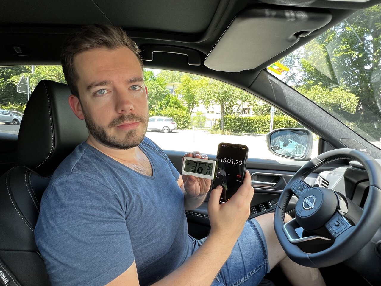 Redaktor Linus Barta mit Thermometer und Telefon in der Hand im Auto