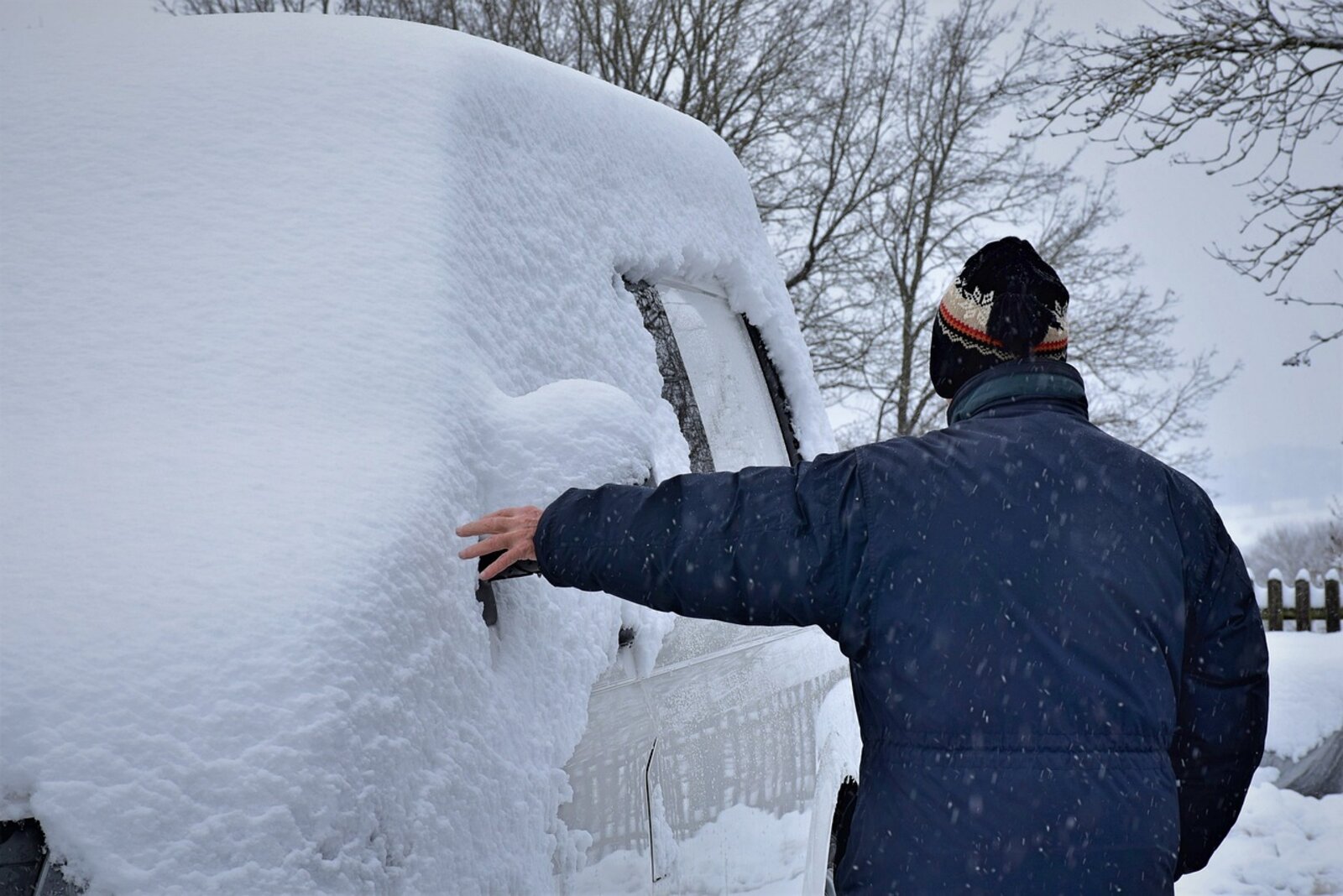 Verschneites Auto und eine Person, die daneben steht.