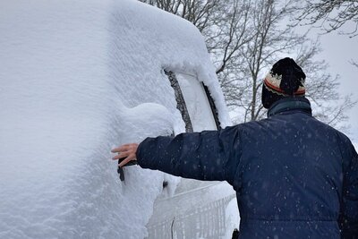 Verschneites Auto und eine Person, die daneben steht.
