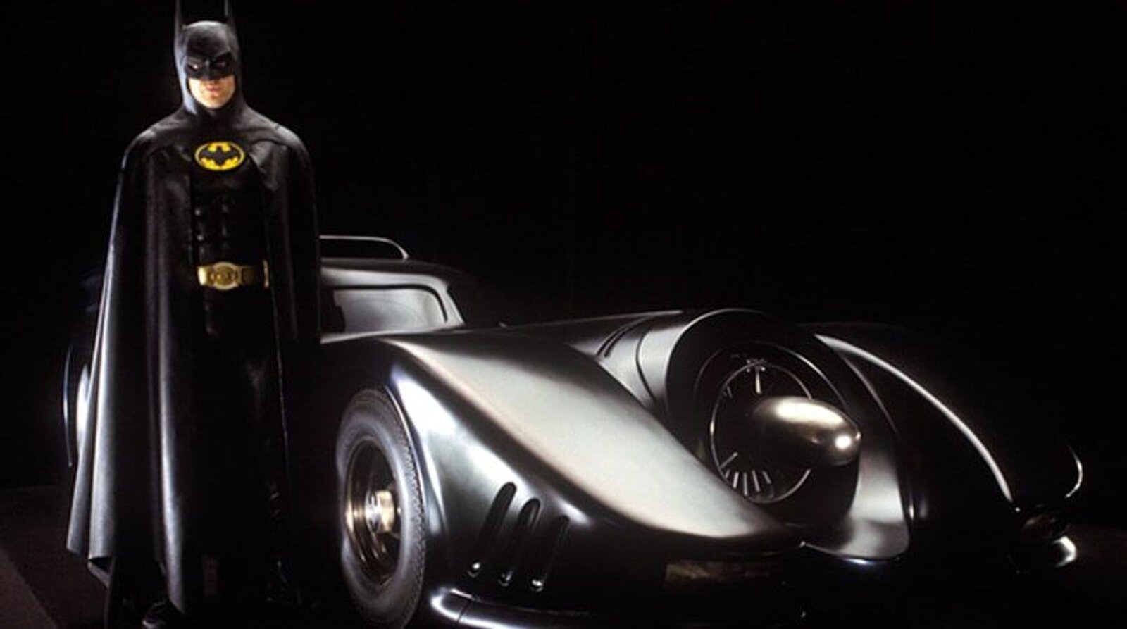 Michael Keaton als Batman neben dem Batmobil aus dem Film von 1989.