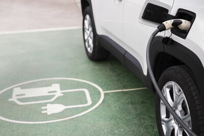 Elektroauto Icon am Boden neben Auto welches eingesteckt ist
